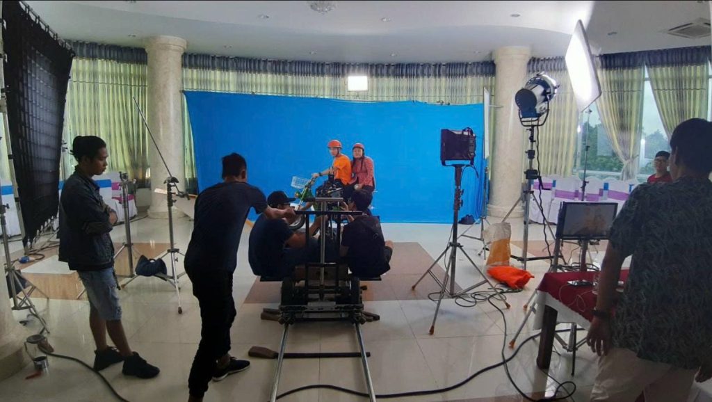 Set quay phông xanh với talent, camera dolly, hệ thống ánh sáng và ekip production.